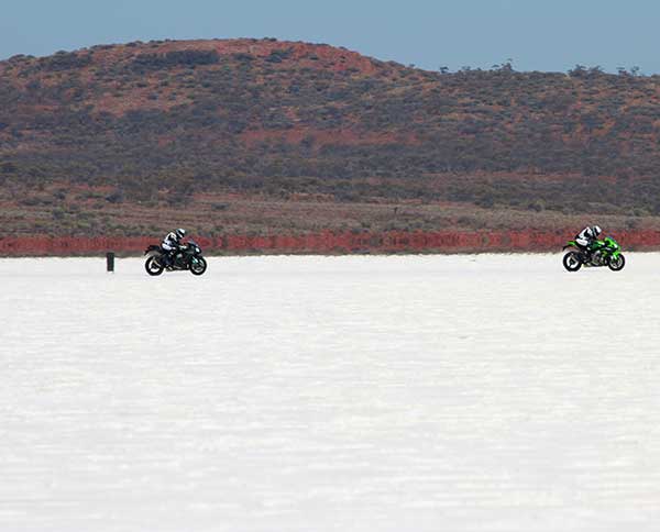 2 motorbikes racing on salt with red hills in the background